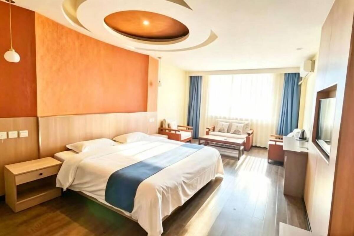 Une chambre d’hôtel comprenant un lit, une table de chevet, un bureau, une chaise et une grande fenêtre avec des rideaux.