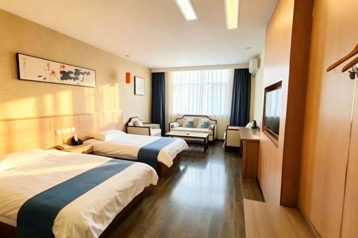 Une chambre d’hôtel avec deux lits, un bureau, une chaise, une télévision et un tableau au mur.