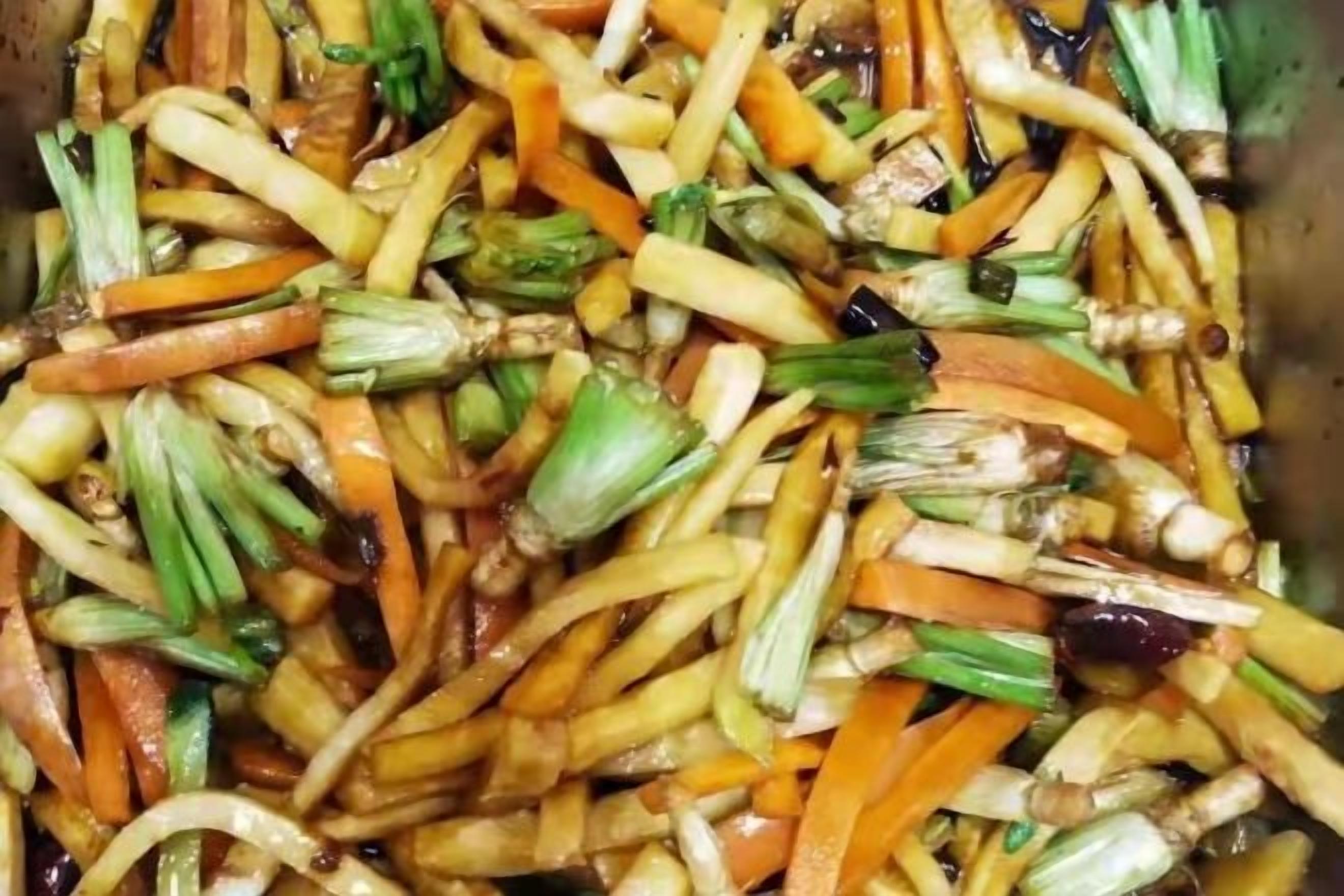 A close-up of a stir-fried vegetable dish with carrots, green onions, and possibly other vegetables.