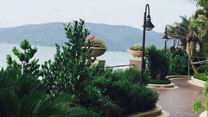 A pathway surrounded by lush greenery and potted plants, leading towards a body of water with mountains in the background. - Double Moon Bay Beach Five Star Resort Apartment (Huidong)