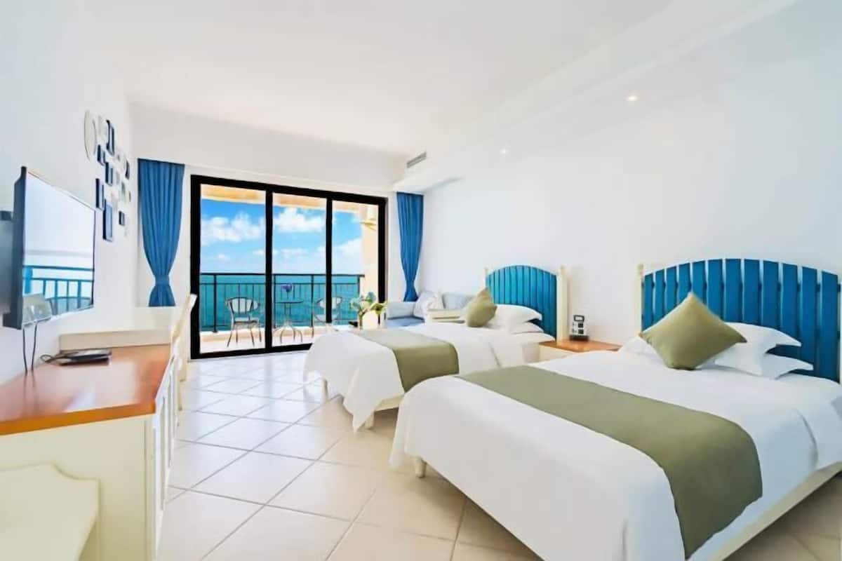 A hotel room with two beds, a desk, and a balcony with a view.