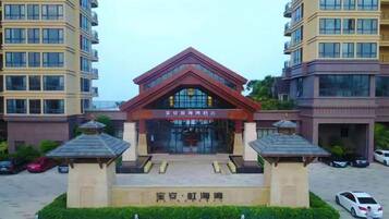 A building with a central entrance, flanked by two smaller structures, and a parking area with cars.