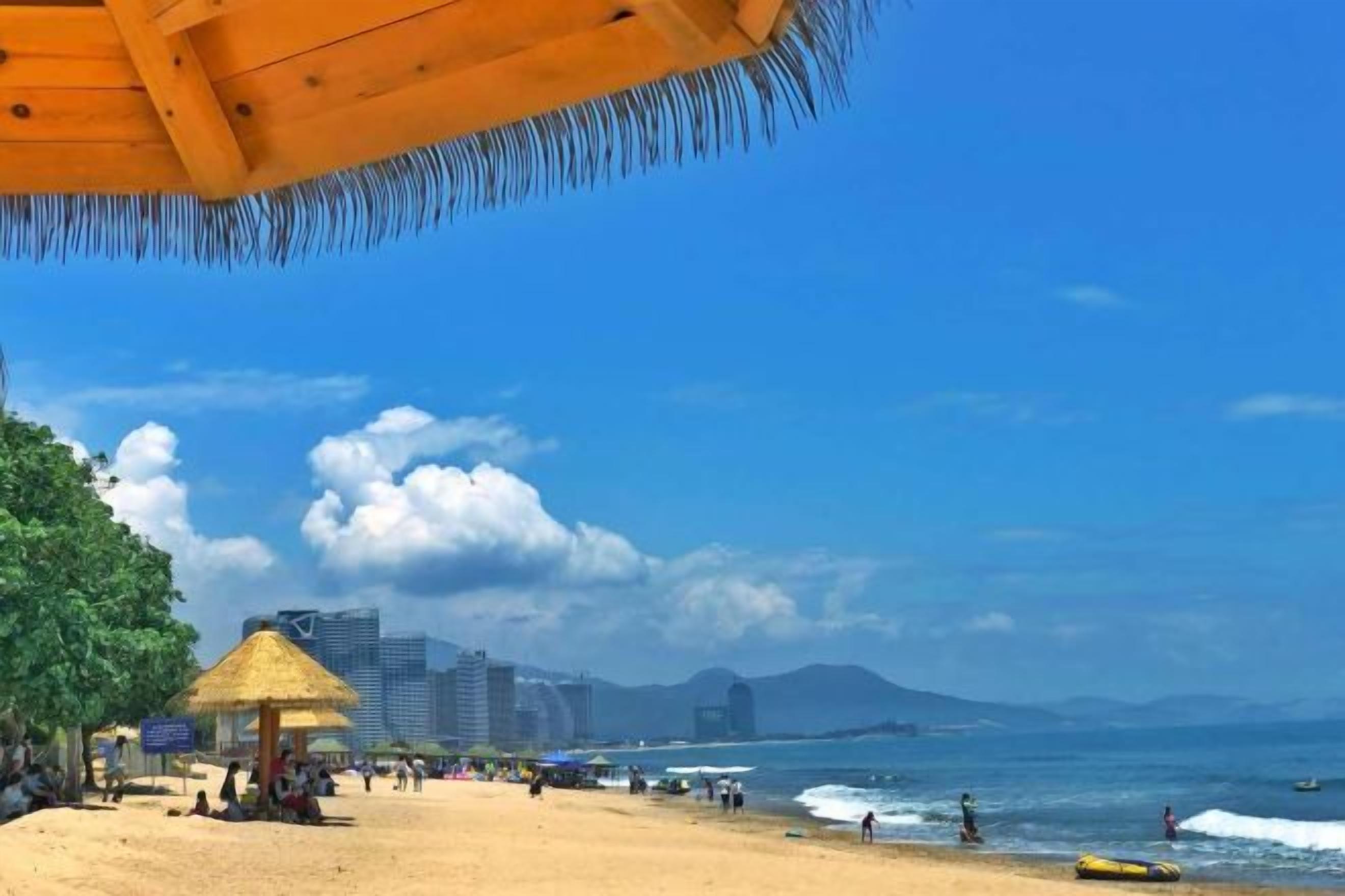 A beach with a thatched-roof structure, a sandy shore, and a clear blue sky.