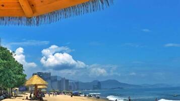A beach with a thatched-roof structure, a sandy shore, and a clear blue sky.