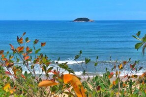 A coastal view with a small island in the distance, clear blue sky, and vegetation in the foreground. - Double Moon Bay Beach Five Star Resort Apartment (Huidong)