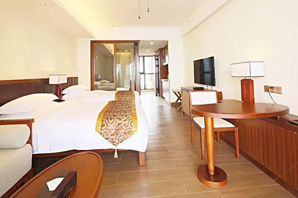 A hotel room with a large bed, a desk with a chair, a television, and a dining area with a table and chairs.