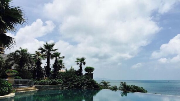 A poolside view with a clear sky, palm trees, and a view of the ocean. - Double Moon Bay Beach Five Star Resort Apartment (Huidong)