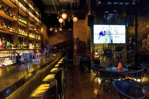 Un'area bar con scaffali pieni di bottiglie, uno schermo televisivo e posti a sedere.