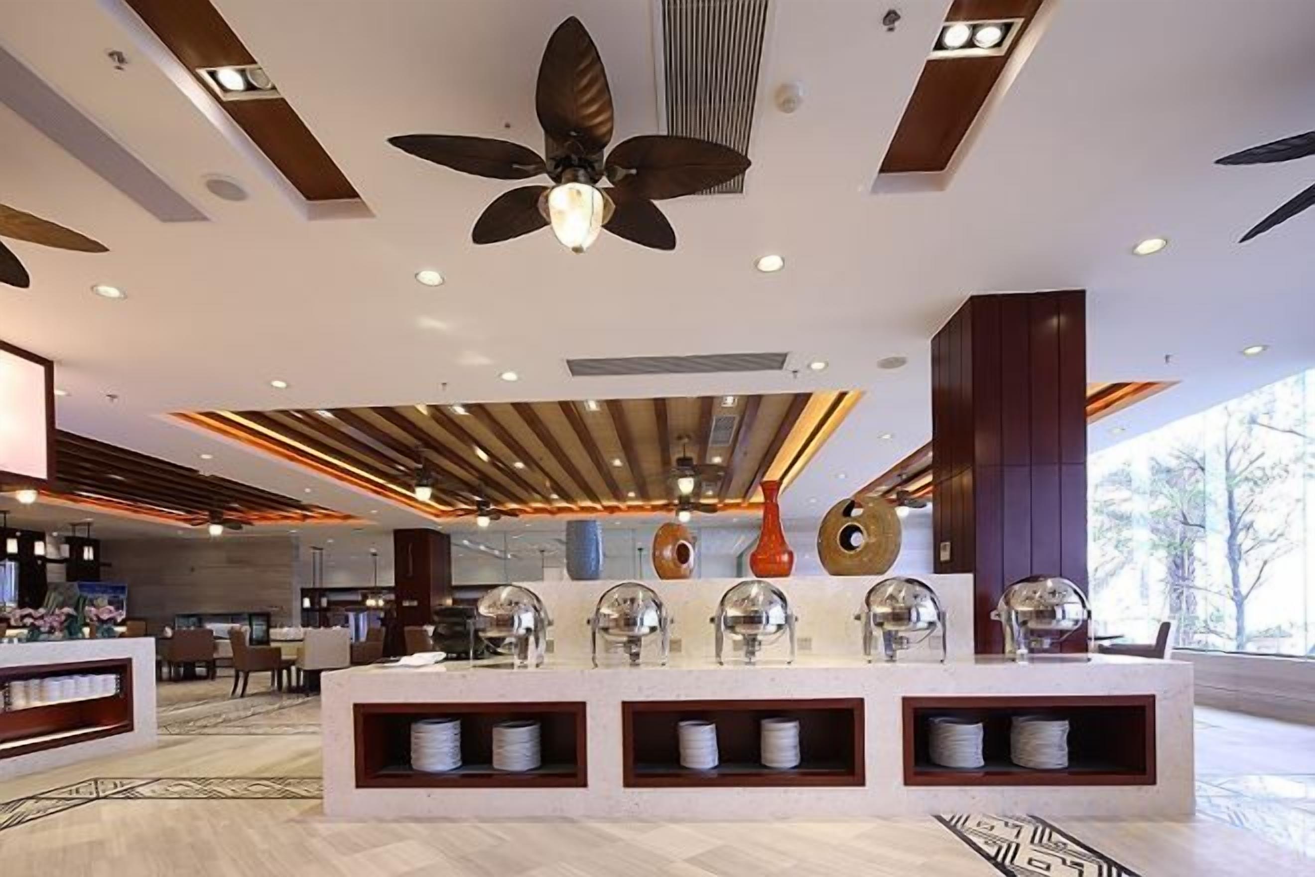 Un moderno vestíbulo de hotel con una recepción central, ventiladores de techo y jarrones decorativos.