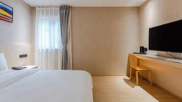 A hotel room with a bed, a desk with a chair, a television, and a window with curtains.
