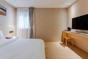 Ein Hotelzimmer mit Bett, Schreibtisch mit Stuhl, Fernseher und einem Fenster mit Vorhängen.