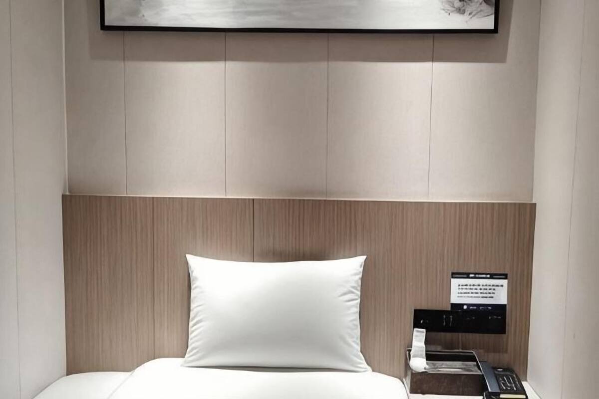 Une chambre d’hôtel avec un lit, une tête de lit, une table de chevet avec un téléphone et un panneau accroché au mur.