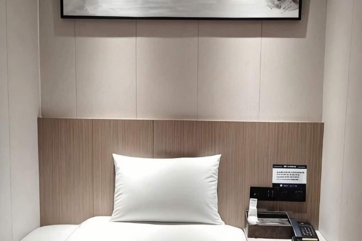 A hotel room with a bed, a headboard, a bedside table with a phone, and a sign on the wall.