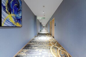 A hotel corridor with a patterned carpet, a large abstract painting on the left wall, and doors on the right. - Allston Light Hotel (Xiamen Gaoqi Airport & Wuyuan Bay) (Xiamen)