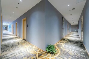 A hotel corridor with a patterned carpet, doors on both sides, and a plant at the corner. - Allston Light Hotel (Xiamen Gaoqi Airport & Wuyuan Bay) (Xiamen)