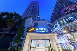 L'ingresso di un hotel con una moderna facciata in vetro, un evidente cartello con su scritto 'All Stone Hotel' e un edificio alto sullo sfondo.