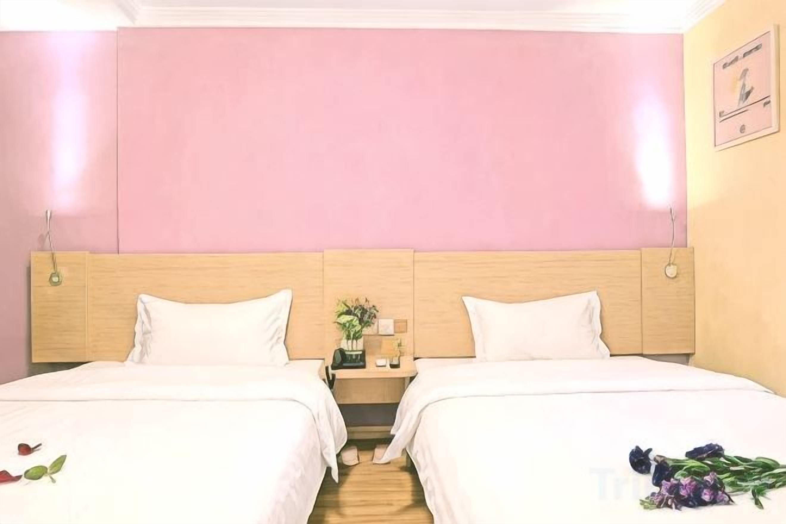 A hotel room with two beds, a wooden headboard, a nightstand with a lamp, and a wall-mounted picture.