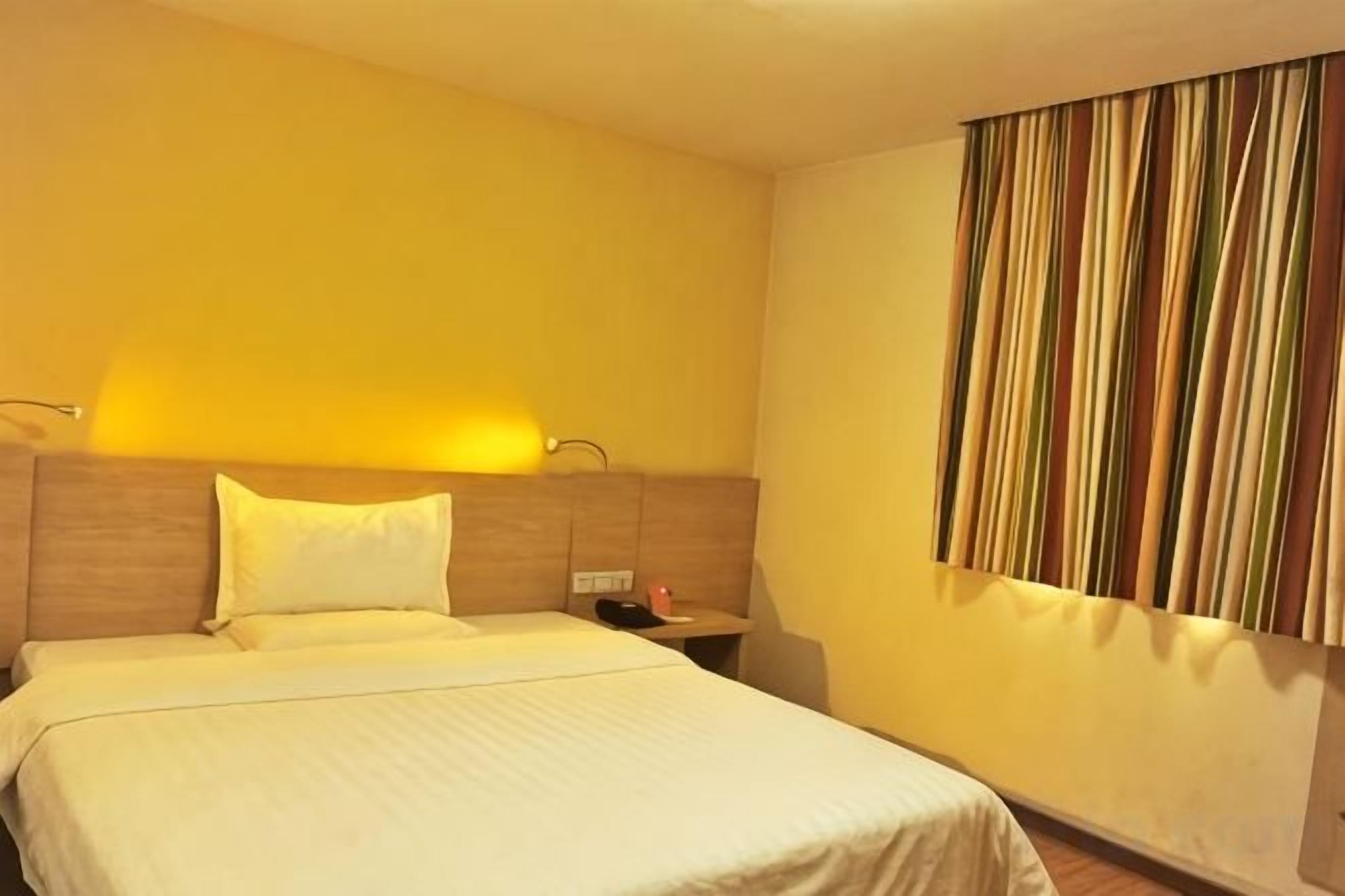 A hotel room with a bed, bedside table, and a wall-mounted curtain.