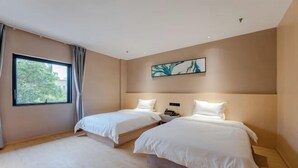 Une chambre d’hôtel avec deux lits, une fenêtre avec des rideaux, un tableau au mur et un plancher en bois.