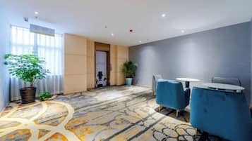 A hotel lobby with a patterned carpet, blue chairs, a reception desk, and potted plants.