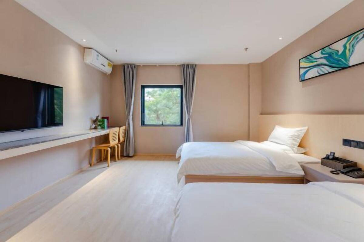Une chambre d’hôtel moderne dotée d’un grand téléviseur à écran plat, d’une fenêtre avec des rideaux, d’un lit, d’une table de chevet et d’une chaise.