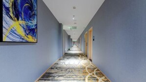 Un long couloir étroit, doté d’un revêtement de sol à motifs et d’un grand tableau abstrait accroché au mur gauche.