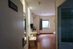 Ein Hotelzimmer mit Holzboden, einem Schreibtisch mit Stuhl, einem Fernseher und einem Fenster mit Vorhängen.