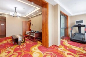Habitación de hotel con una cinta caminadora, una mesita con una bandeja, una silla y una alfombra estampada.
