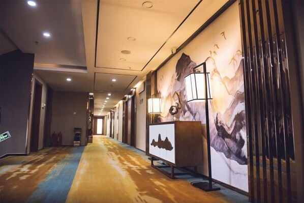 A hotel corridor with a wooden floor, a reception desk with a mountain painting, and a wall with a similar painting.