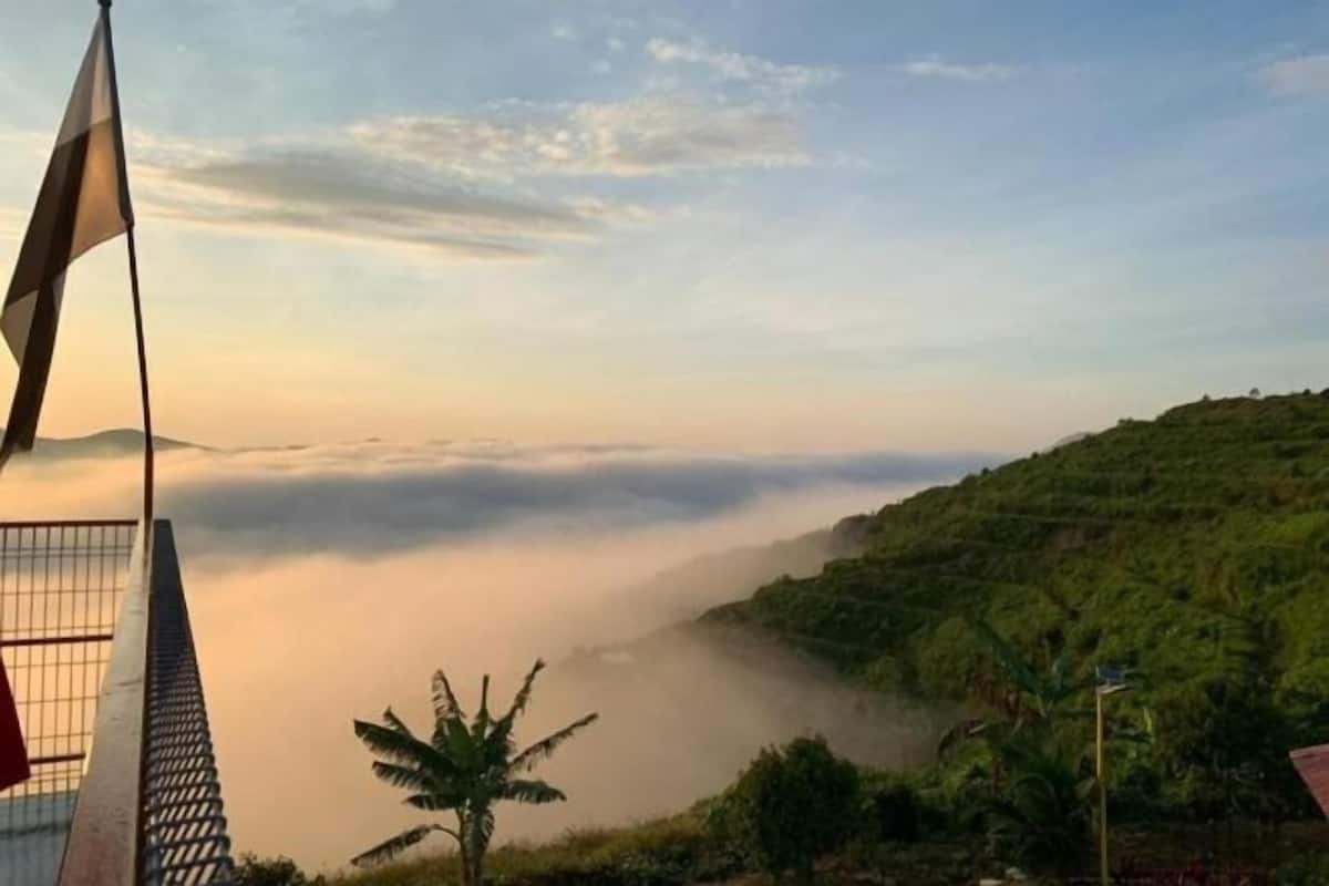 A view of a building with a flagpole, surrounded by lush greenery and a misty landscape.