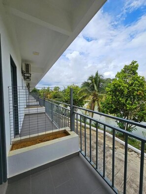 A balcony with a metal railing, a staircase, and a view of greenery and a body of water.