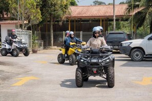 A group of people on quad bikes in a parking area with a building in the background.