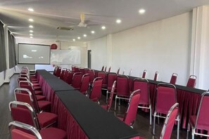 Une salle de conférence avec une longue table, des chaises rouges, un écran de projection et un tableau blanc.