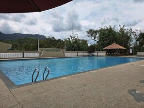 A swimming pool with a tiled deck, a covered seating area, and a fence with a sign.