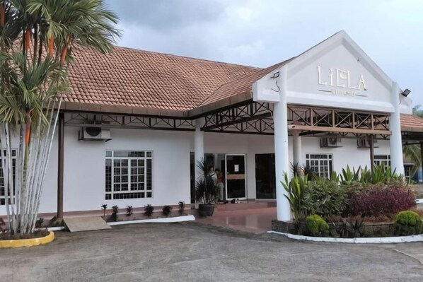 A building with a white facade and a red-tiled roof, featuring a covered entrance area with a sign that reads 'LIELA.'