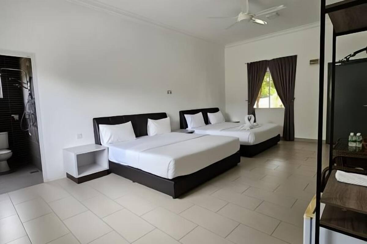 A hotel room with two beds, a ceiling fan, a window with curtains, and a small bedside table.