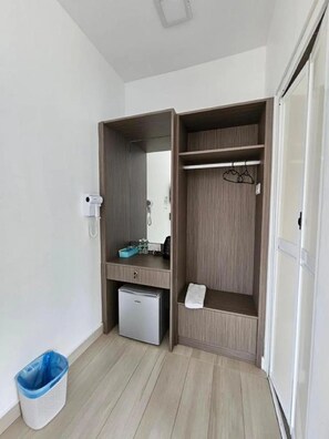 A compact room with a built-in wardrobe, a small refrigerator, and a trash bin.