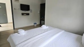 Habitación de hotel con dos camas, televisión, refrigerador pequeño y un basurero.