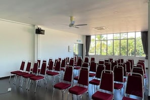 A conference room with rows of red chairs, a ceiling fan, and large windows.