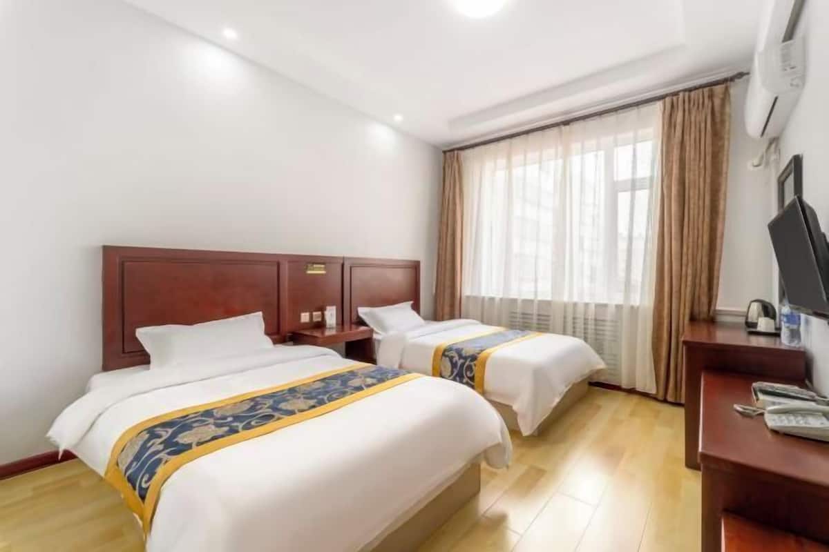 Ein Hotelzimmer mit zwei Betten, einem Schreibtisch, einem Stuhl und einem Fenster mit Vorhängen.