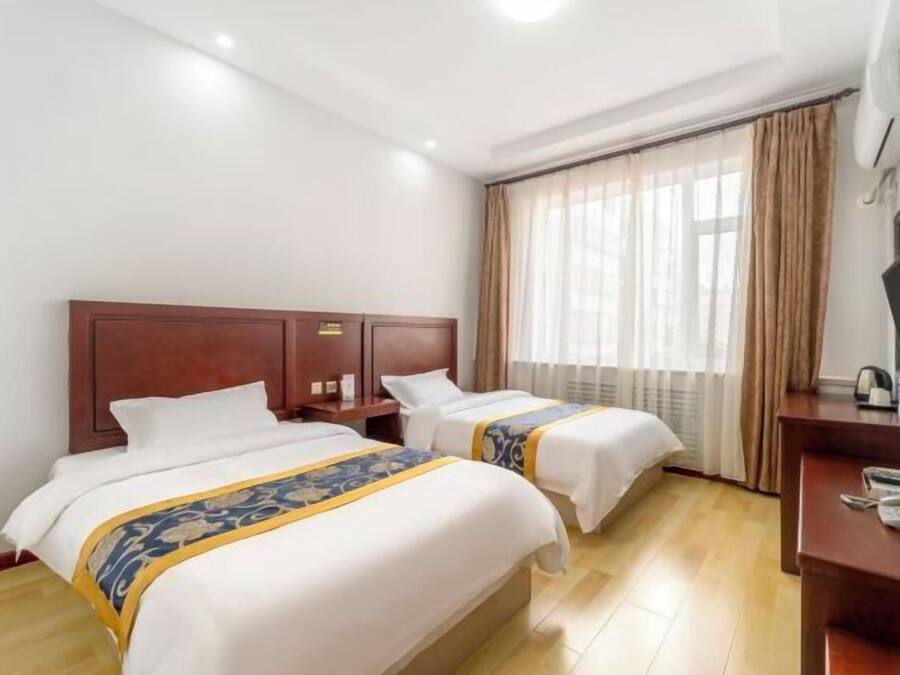 A hotel room with two beds, a desk, a chair, and a window with curtains.
