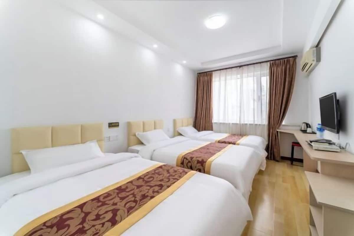 A hotel room with three beds, a desk, a television, and a window with curtains.