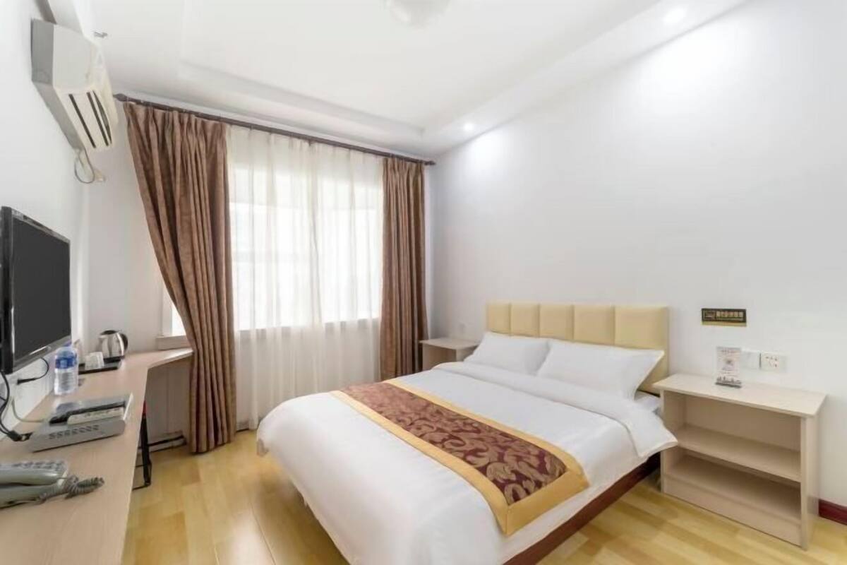A hotel room with a bed, a desk with a computer, a TV, and a window with curtains.