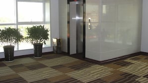 Un ascenseur avec un panneau rouge portant le chiffre 4, une colonne en marbre et un tapis à motifs.