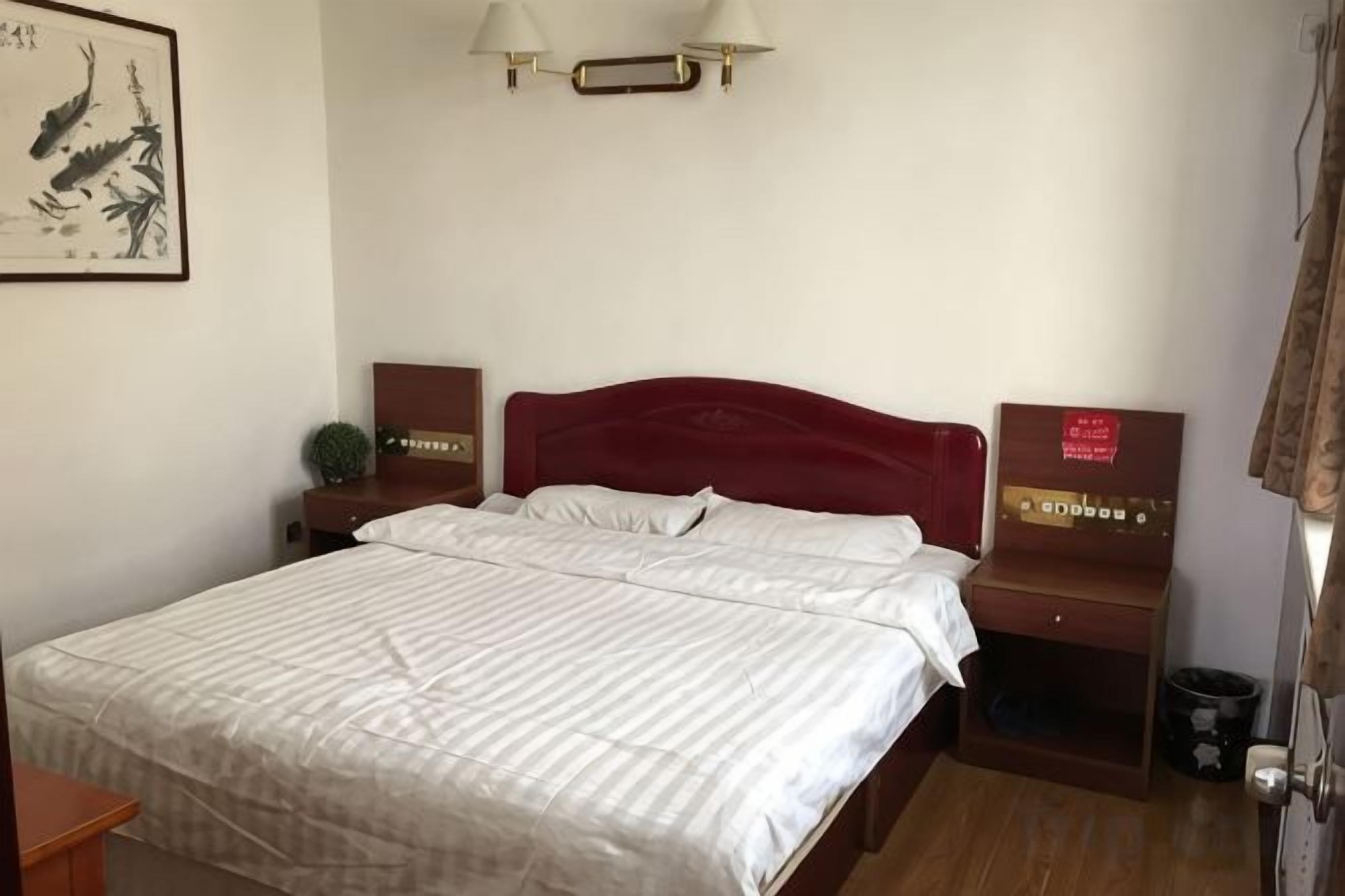 A hotel room with a bed, bedside tables, a nightstand, a wall-mounted lamp, and a framed picture.
