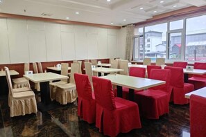 A restaurant with tables and chairs, large windows, and a view of buildings outside. - Jingxuanlou Hotel（near the great wall） (Qinhuangdao)