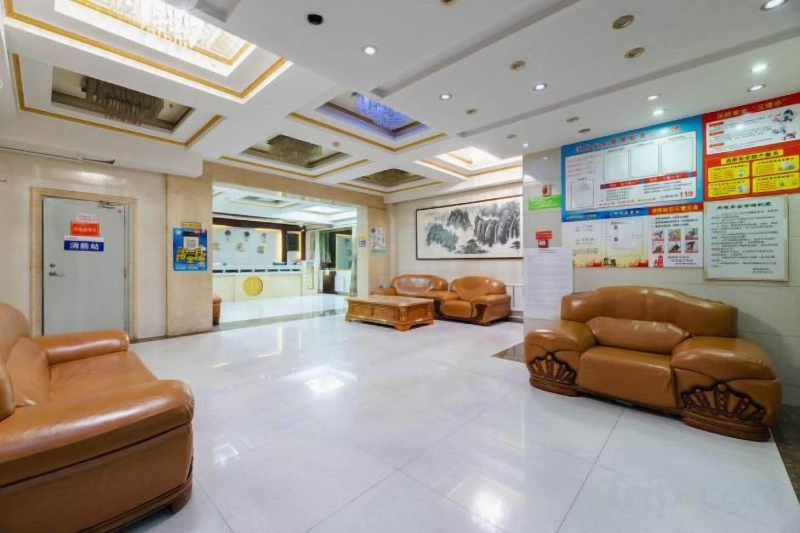 A hotel lobby with leather seating, a reception desk, and informational posters on the walls.