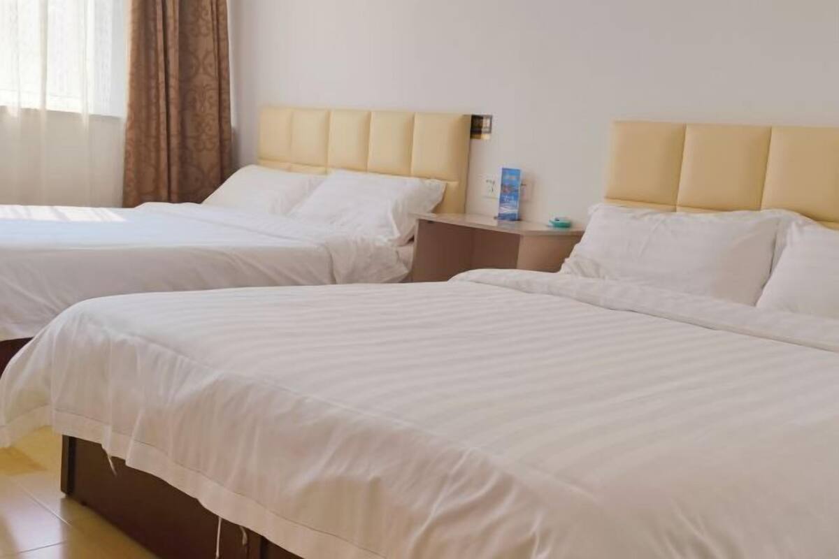 A hotel room with two beds, a nightstand, and a window with curtains.