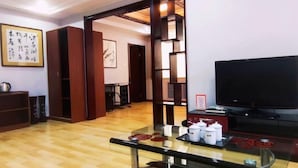Un salon avec un plancher en bois, une table basse en verre, un téléviseur et une bibliothèque.