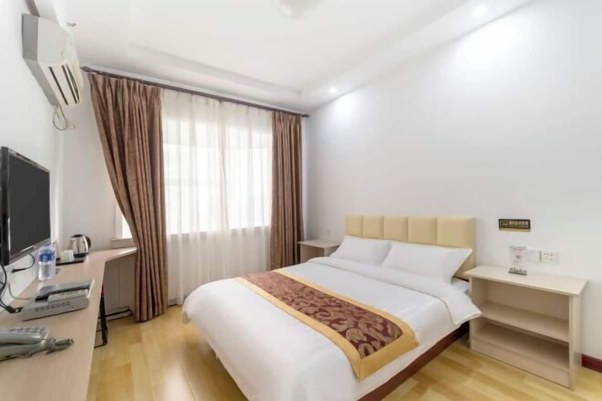 A hotel room with a bed, a desk with a computer, a TV, and a window with curtains.